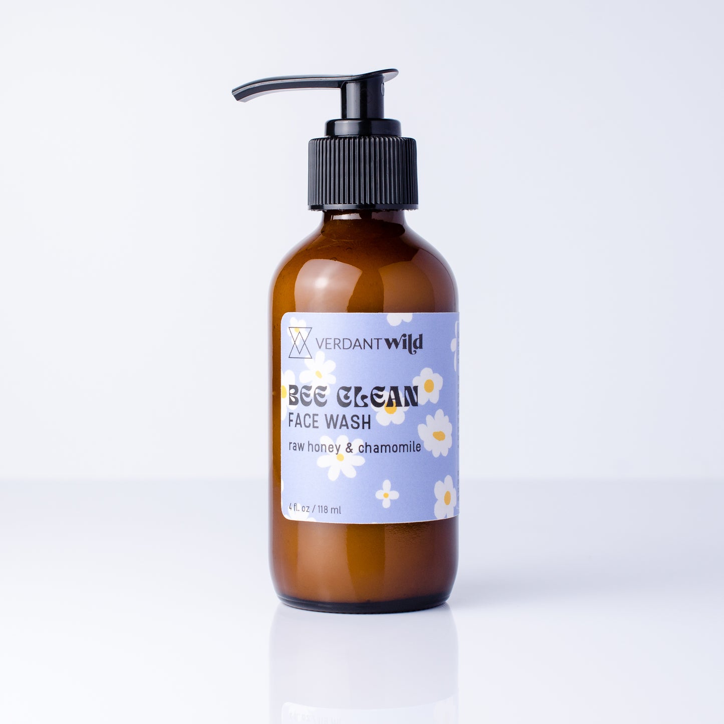 A bottle of Verdant Wild Bee Clean Face Wash in an amber glass bottle with a black pump dispenser and a light blue label decorated with white chamomile flowers, set against a clean white background.