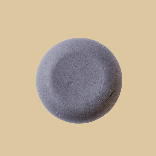 A round, smooth gray conditioner bar photographed from above on a plain white background.