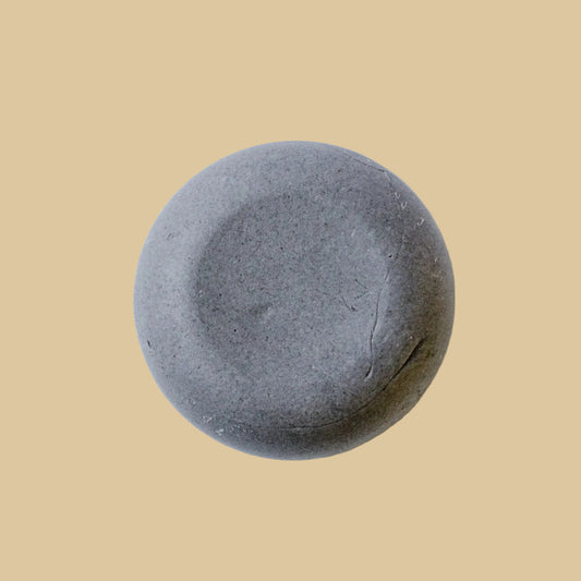 A round, smooth gray conditioner bar photographed from above on a plain background.