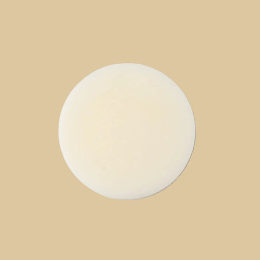 A single round, pale cream-colored conditioner bar, centered on a clean white background.