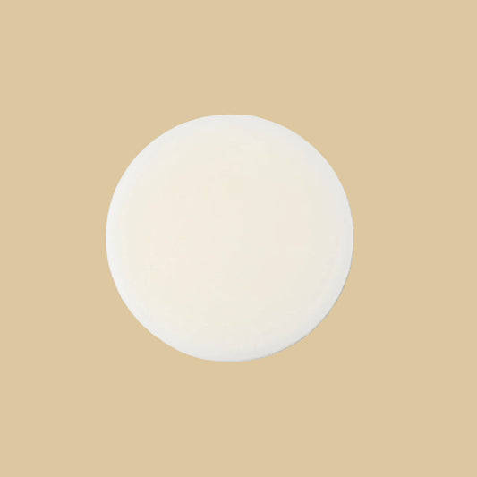 A round, solid bar of conditioner in a cream color, photographed from directly above on a clean background.