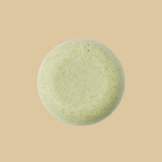 A single round, pale sage green shampoo bar with a textured, matte surface, photographed from directly above on a plain background.
