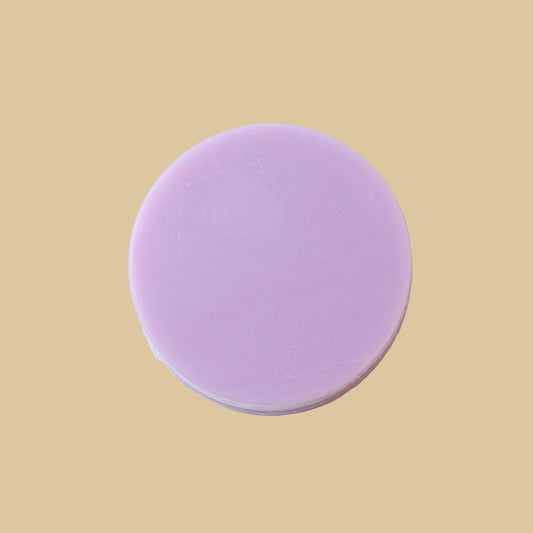 A round, solid bar of lavender conditioner, photographed from directly above on a clean background.