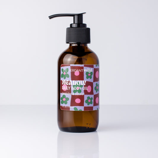 An amber glass pump bottle of 'Meadow' Daily Body Oil with a black pump dispenser and a colorful patterned label, set against a clean white background.