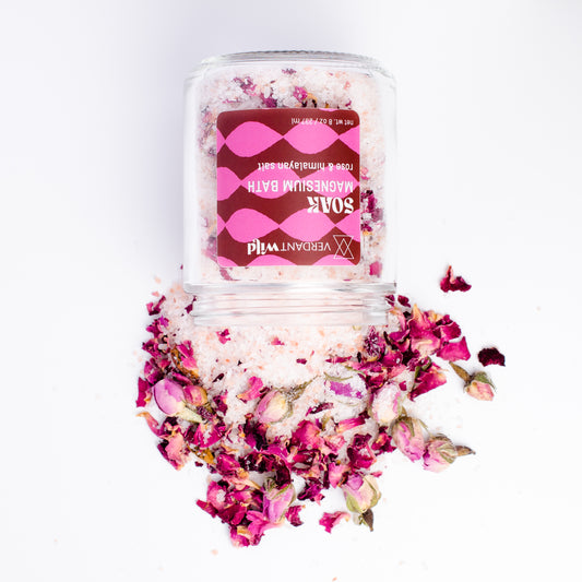 A clear jar of Vegvirital Wild 'Soak' rose bath salts with a pink label, shown on a white background with dried rose petals spilled around the base.