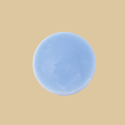 A round, light blue conditioner bar, photographed from directly above on a clean background.
