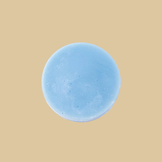 A round, light blue conditioner bar, photographed from directly above on a clean background.