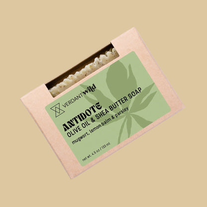 A rectangular kraft paper box of Verdant Wild Antidote Olive Oil & Shea Butter Soap. The box features a light green label with black text and a leaf graphic, and a small window at the top reveals the olive green soap bar inside.