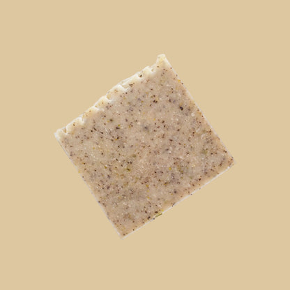 A single square bar of speckled olive green soap, photographed from above on a clean beige background.
