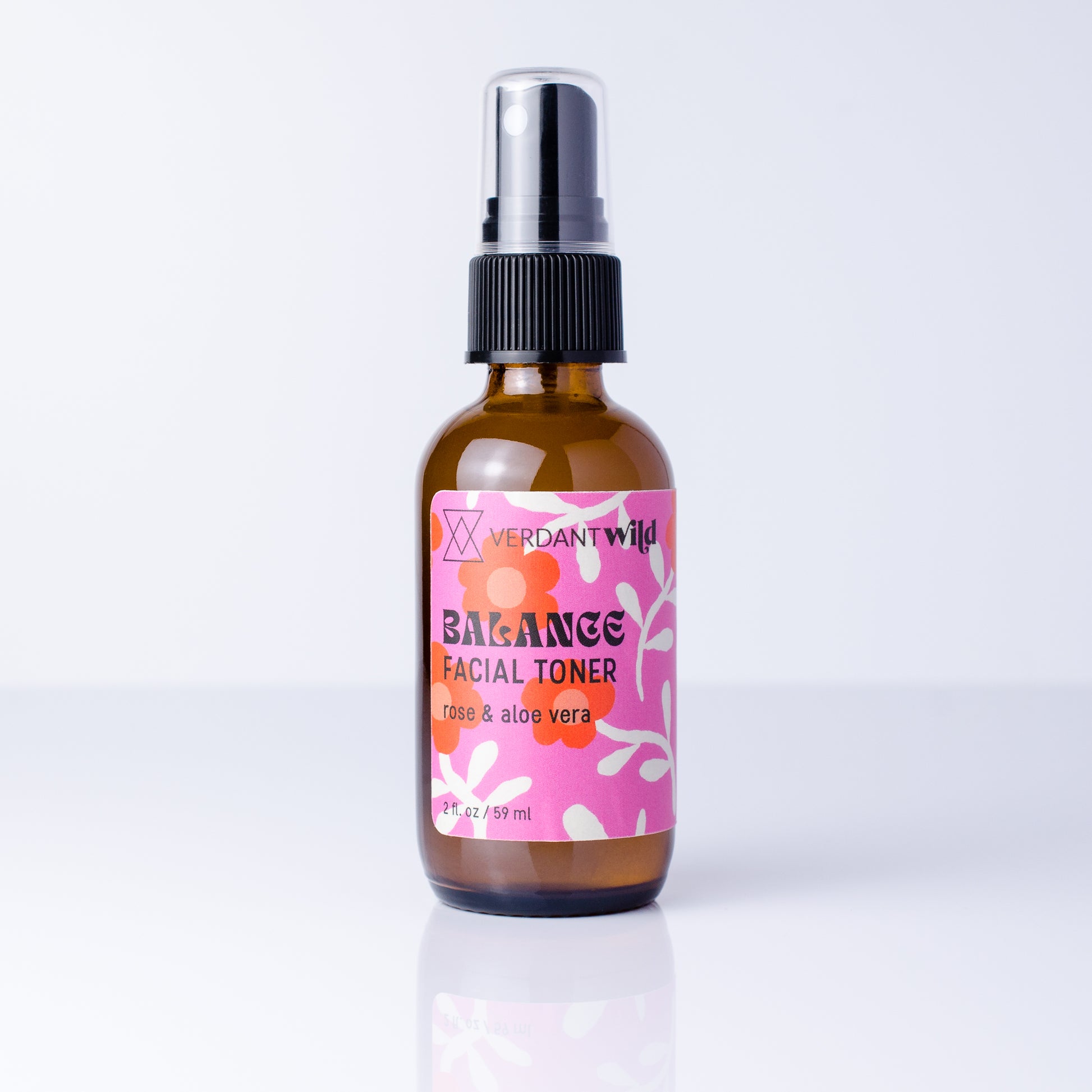 A 2 fl oz amber glass spray bottle of Verdant Wild Balance Facial Toner with a pink and orange label, set against a clean white background with a soft reflection.