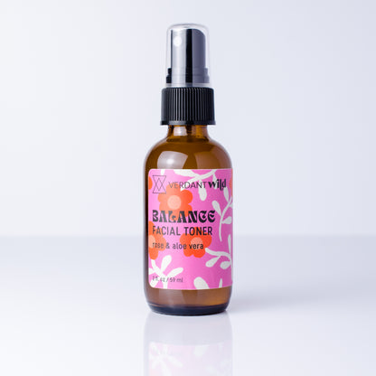 A 2 fl oz amber glass spray bottle of Verdant Wild Balance Facial Toner with a pink and orange label, set against a clean white background with a soft reflection.