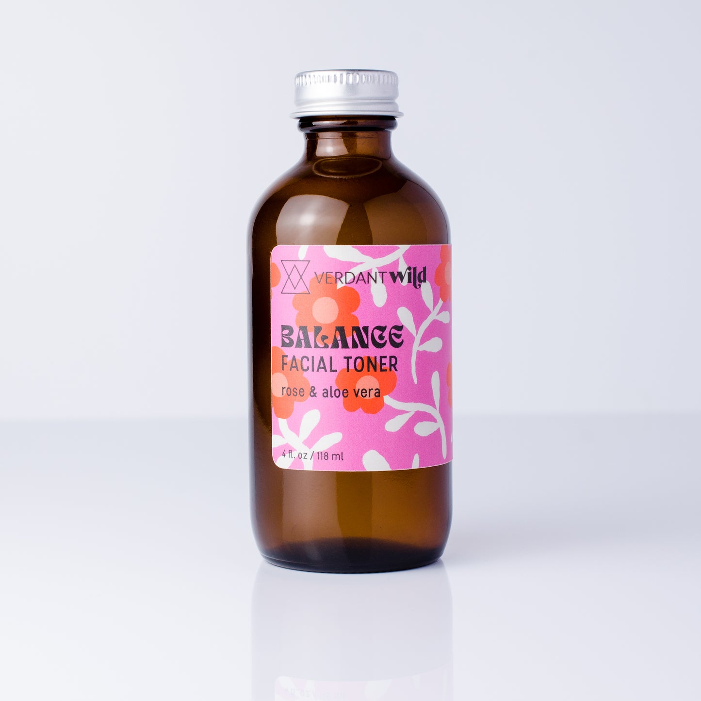 An amber glass bottle of Verdant Wild Balance Facial Toner with a pink floral label and a silver cap, set against a clean white background with a soft reflection.