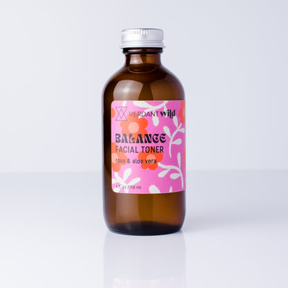 An amber glass bottle of Verdant Wild Balance Facial Toner with a pink floral label and a silver cap, set against a clean white background with a soft reflection.