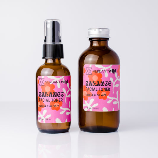 Two amber glass bottles of Verdant Wild Balancer Facial Toner with pink labels, one with a black spray top and one with a silver cap, on a white background.