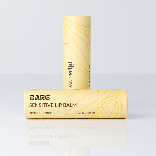 Two tubes of Bare Lip Balm in a pale yellow color with black text and a yellow botanical line drawing, displayed on a reflective white surface against a light gray background.