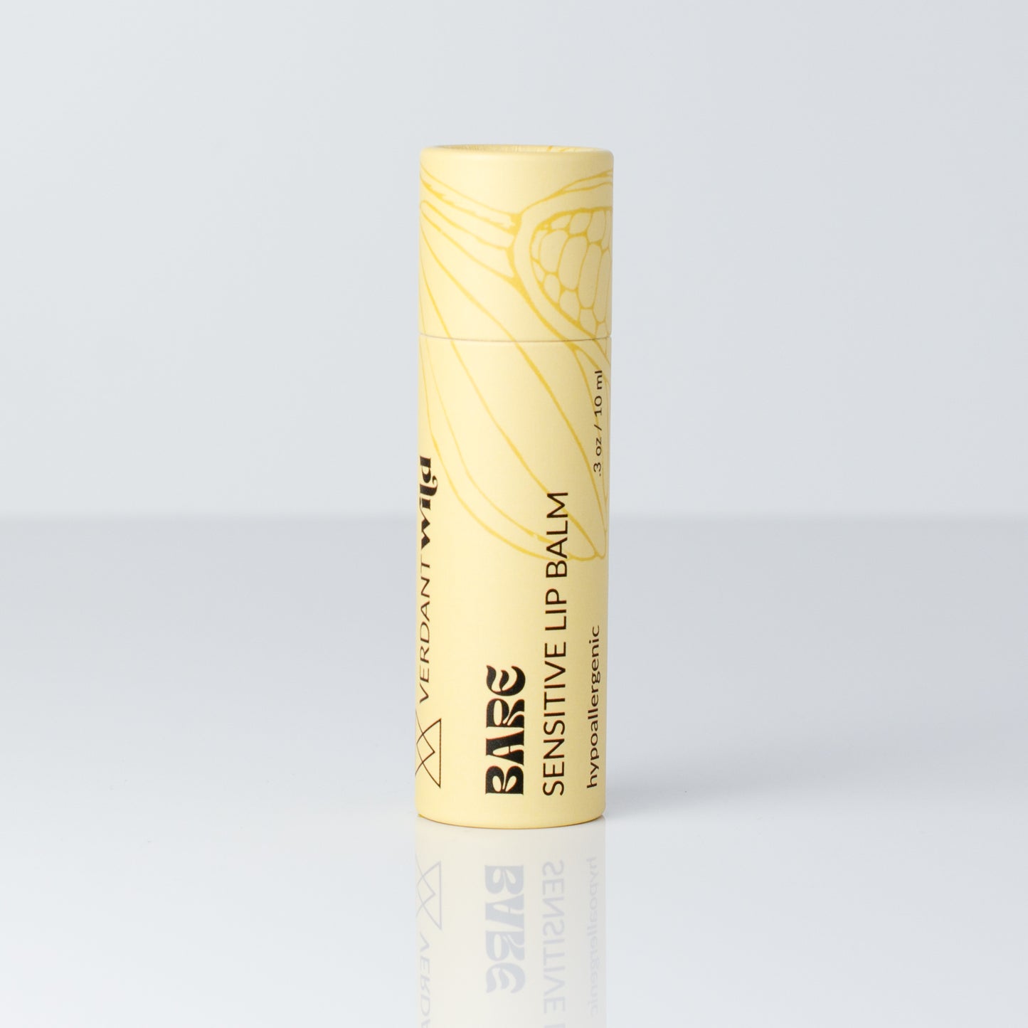 A single tube of Bare Sensitive Lip Balm in a pale yellow color with black text and a botanical line drawing, standing upright on a reflective light gray surface.