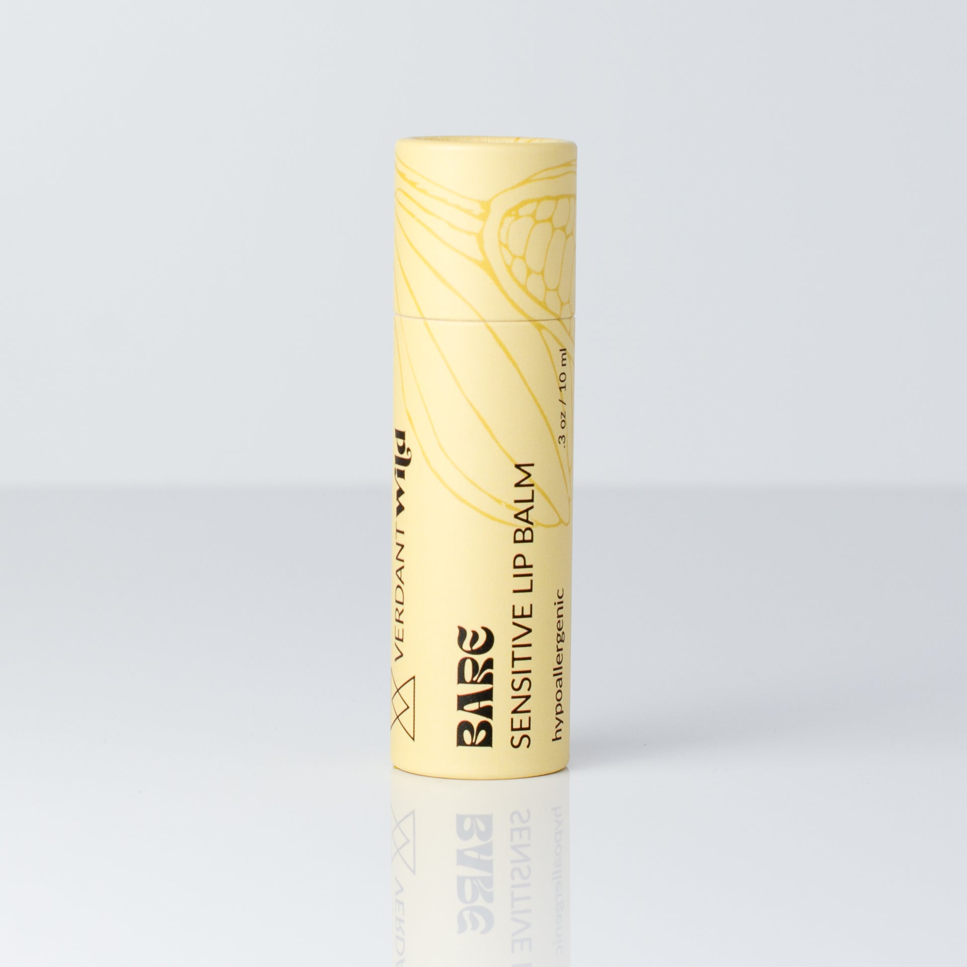A single tube of Bare Sensitive Lip Balm in a pale yellow color with black text and a botanical line drawing, standing upright on a reflective light gray surface.