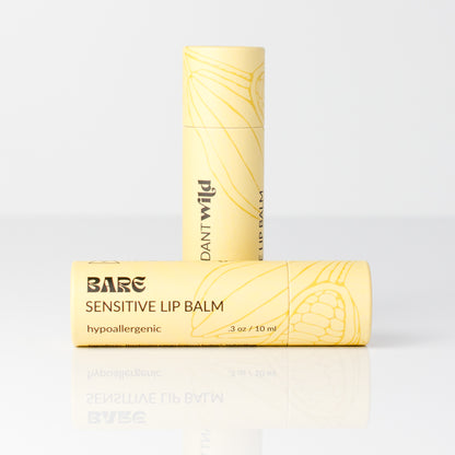 Two pale yellow lip balm tubes on a clean white studio background. One tube stands upright behind the other, which is lying horizontally.