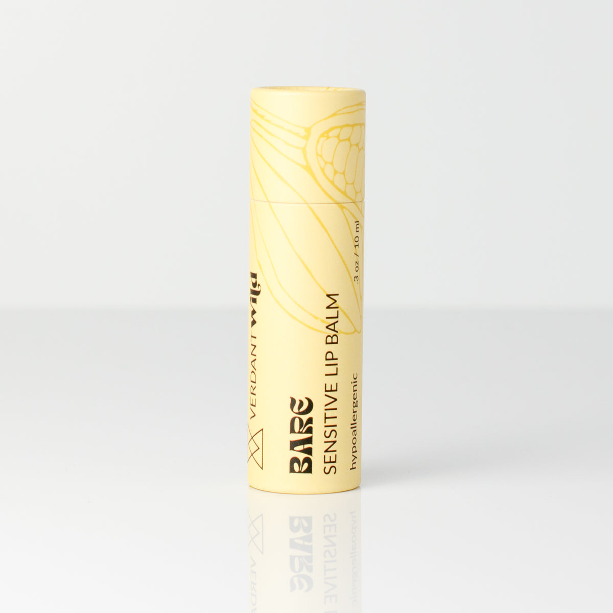 A single tube of Bare Sensitive Lip Balm in a pale yellow color with gold line art and black text, standing upright on a reflective white surface against a white background.