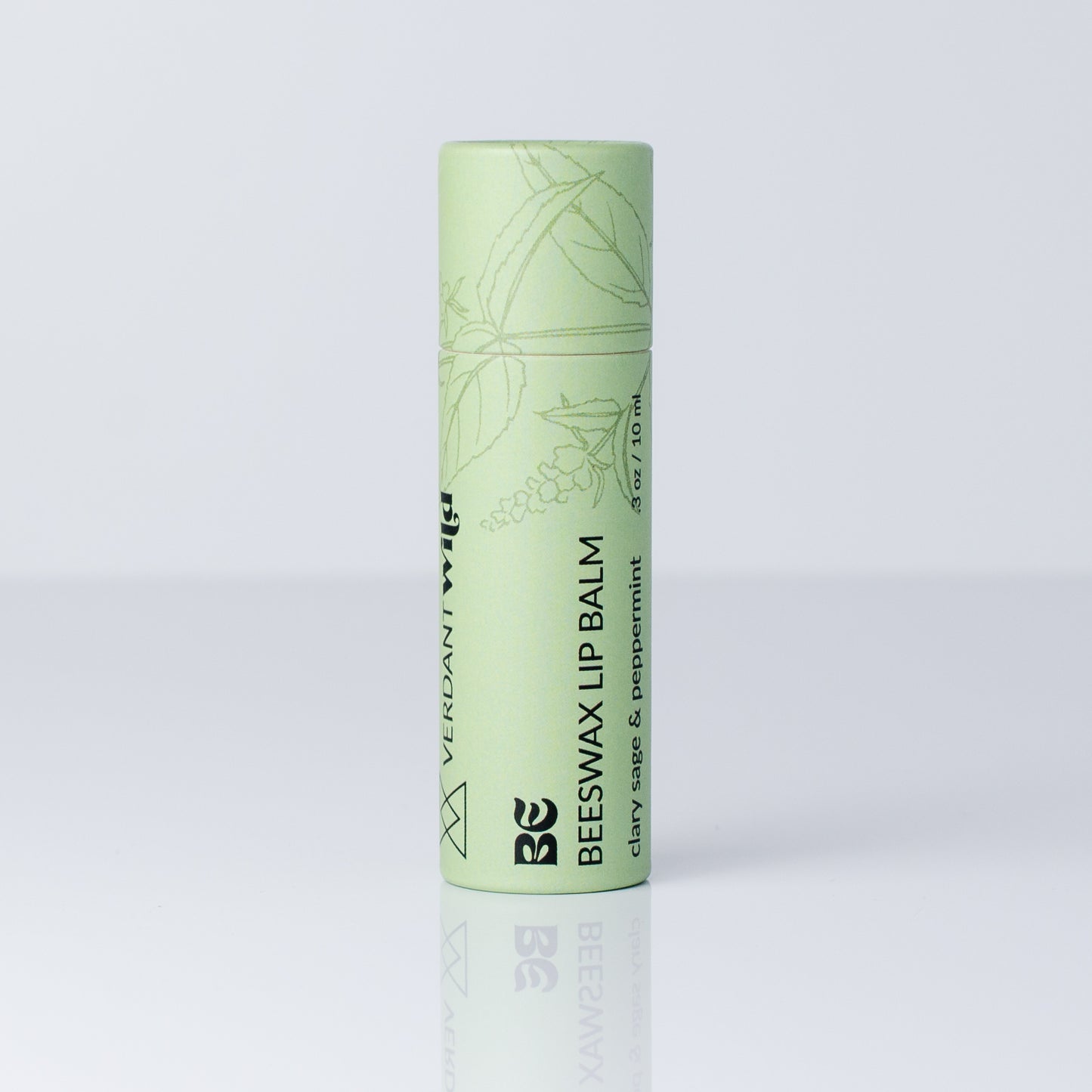 A single tube of Beeswax Lip Balm by Verdant Wild, in a light mint green color with black text and botanical line drawings, standing upright on a reflective white surface against a light gray background.