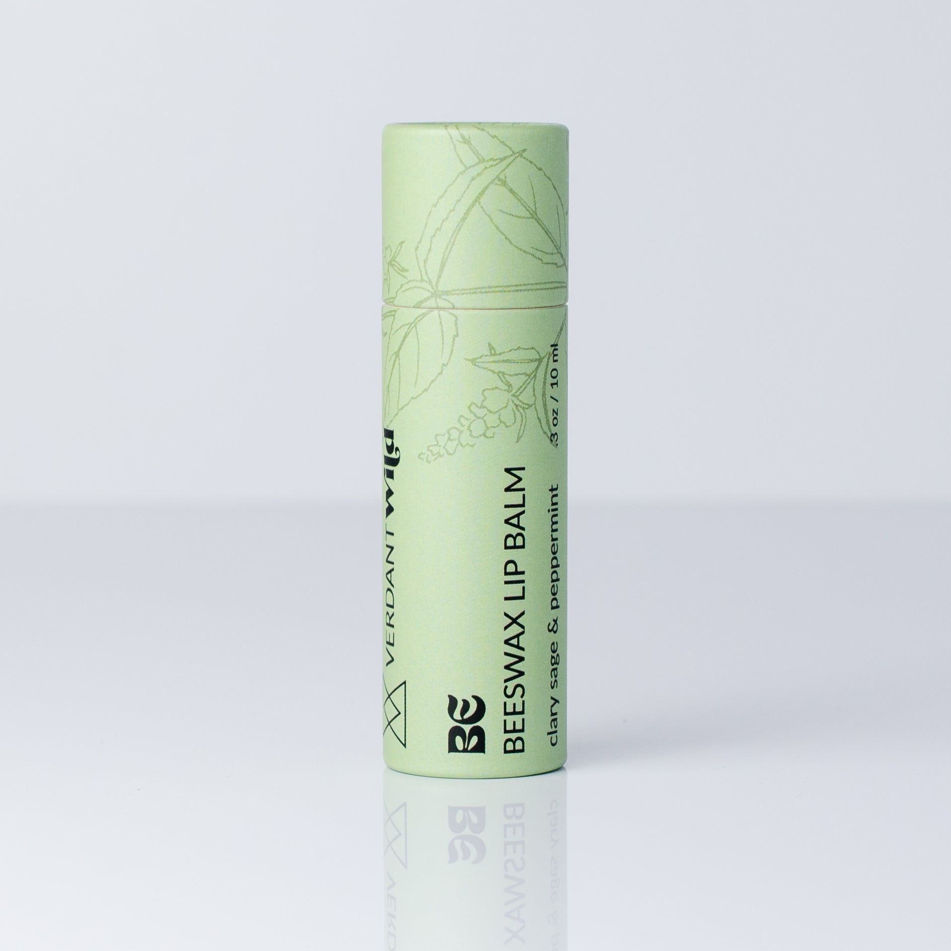 A single tube of Beeswax Lip Balm by Verdant Wild, in a light mint green color with black text and botanical line drawings, standing upright on a reflective white surface against a light gray background.