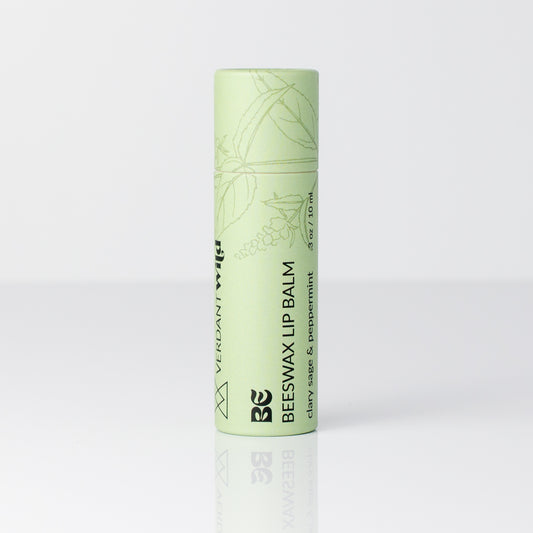 A single tube of Beeswax Lip Balm in a pale mint green color, standing upright on a reflective white surface against a light gray background.