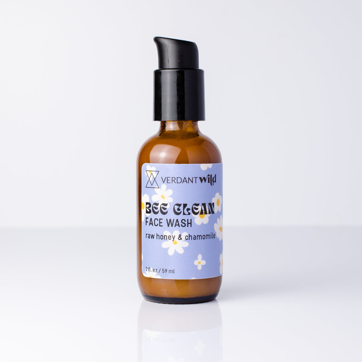 A 2 oz bottle of Verdant Wild Bee Clean Face Wash with a black pump and amber glass bottle, set against a clean white background with a soft reflection.