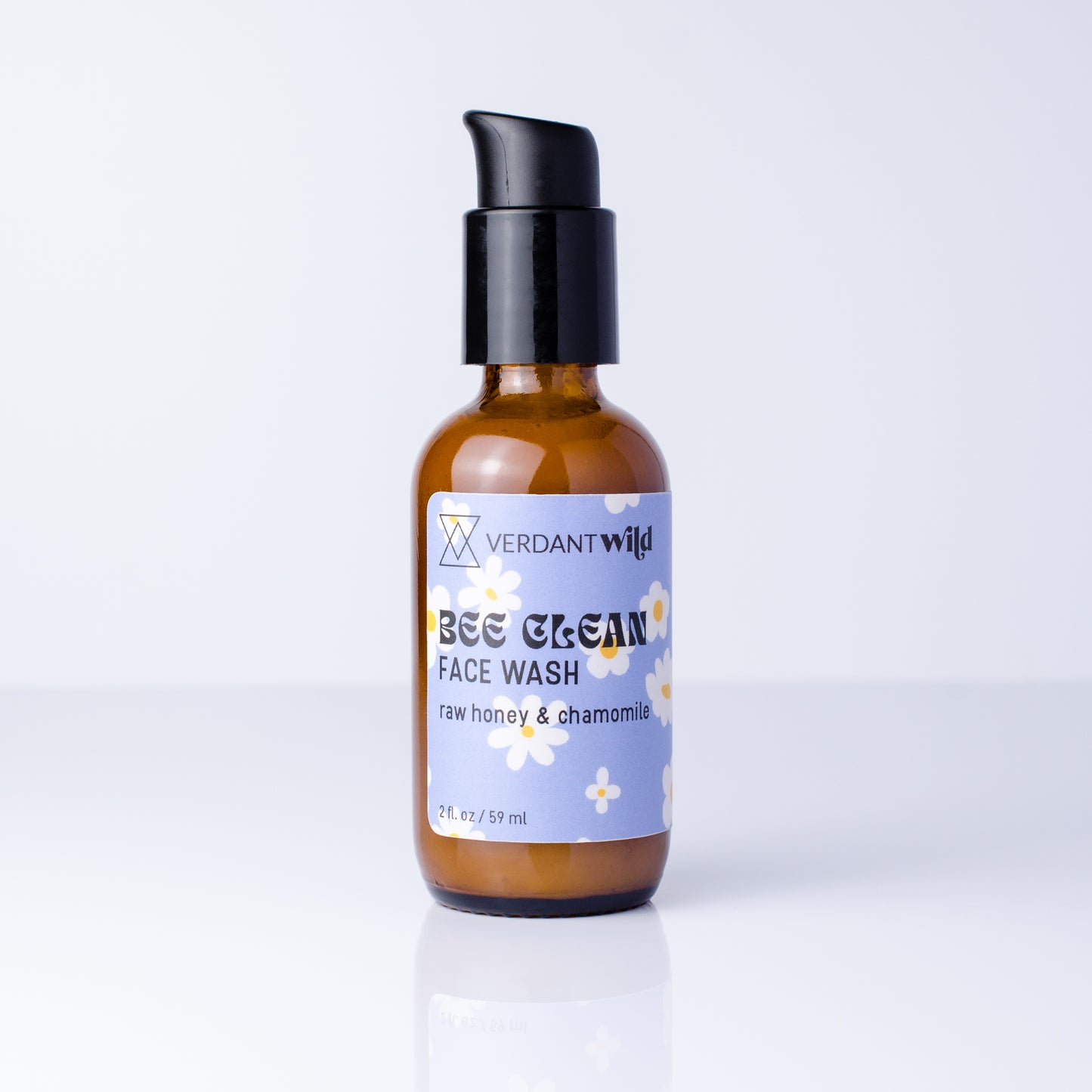 A 2 fl oz amber glass bottle of Verdant Wild Bee Clean Face Wash with a black pump dispenser and a light purple label, set against a clean white background with a soft reflection.