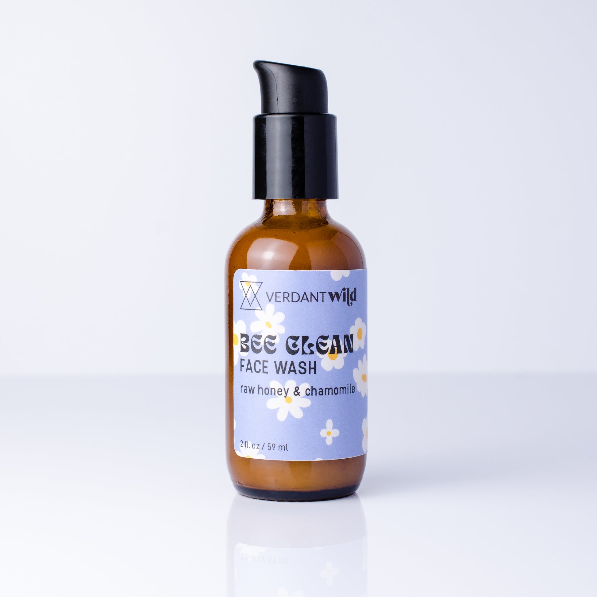 A 2 fl oz amber glass bottle of Verdant Wild Bee Clean Face Wash with a black pump dispenser and a light purple label, set against a clean white background with a soft reflection.
