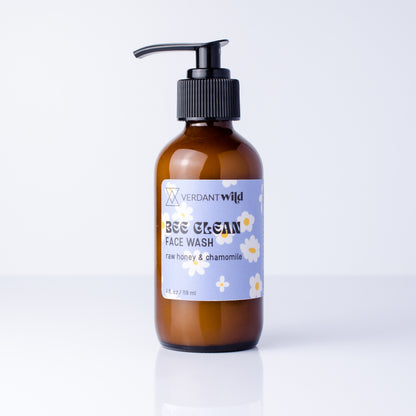 A bottle of Verdant Wild Bee Clean Face Wash in an amber glass bottle with a black pump dispenser and a light blue label decorated with white chamomile flowers, set against a clean white background.