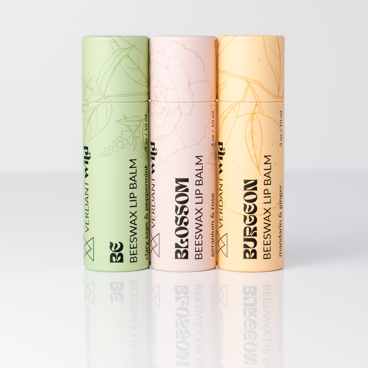 Three vertical tubes of Verdant Wild beeswax lip balm in light green, pale pink, and warm peach, arranged side by side on a clean white reflective surface.