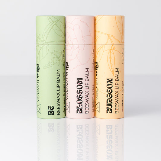 Three vertical tubes of Verdant Wild beeswax lip balm in light green, pale pink, and warm peach, arranged side by side on a clean white reflective surface.