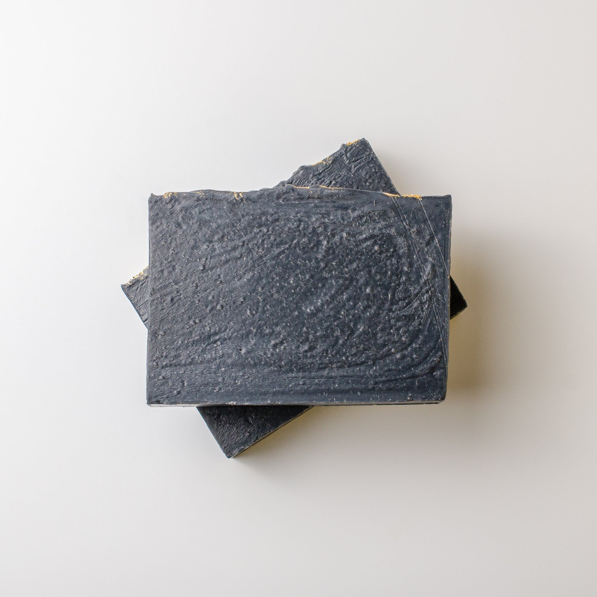 Three bars of dark soap stacked on a light gray background