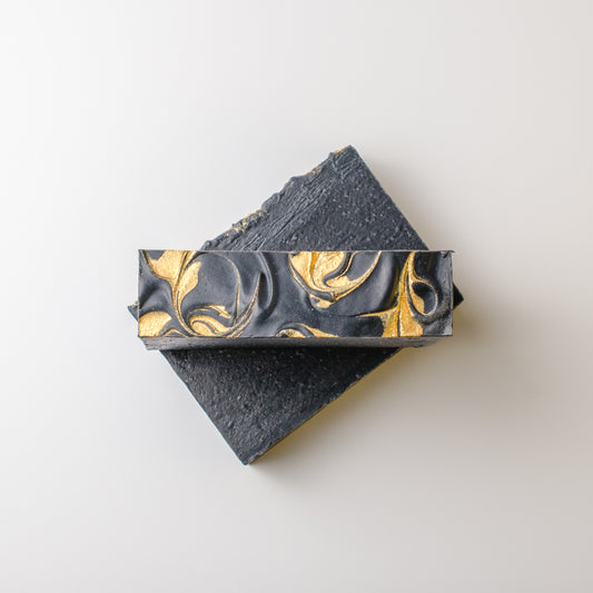 Two bars of black soap with gold marbling on a light gray background