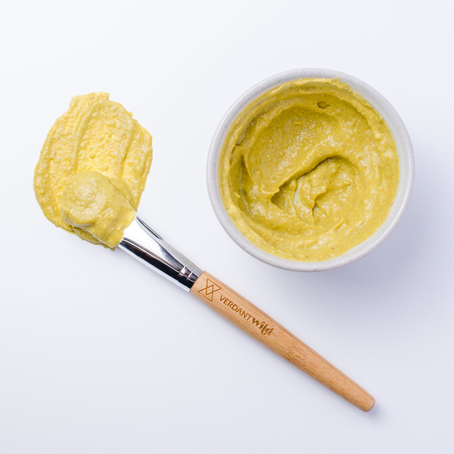 A close-up overhead shot of Verdant Wild Brighten Facial Grains (chamomile & turmeric) mixed up and ready to mask. Pretty yellow color.