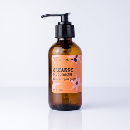A bottle of Verdant Wild Cleanse Oil Cleanser with a black pump dispenser and an amber glass bottle, featuring an orange label with floral designs, set against a clean white background.