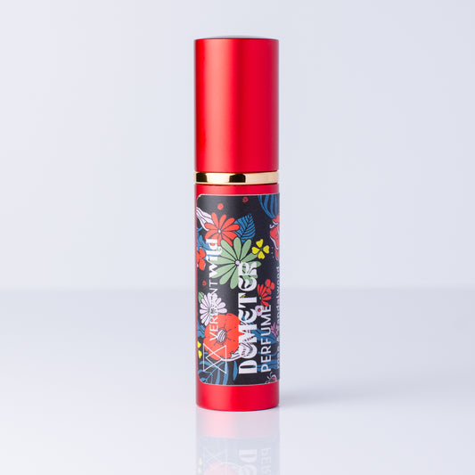 A cylindrical perfume bottle with a metallic red cap and base, a gold band, and a black label decorated with colorful floral illustrations and the text 'DEMETER PERFUME'.