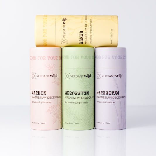 Four Verdant Wild magnesium deodorant paperboard tubes arranged on a white reflective surface. In pastel pink, light green, lavender, and pale yellow, each with black text and a subtle botanical line pattern.