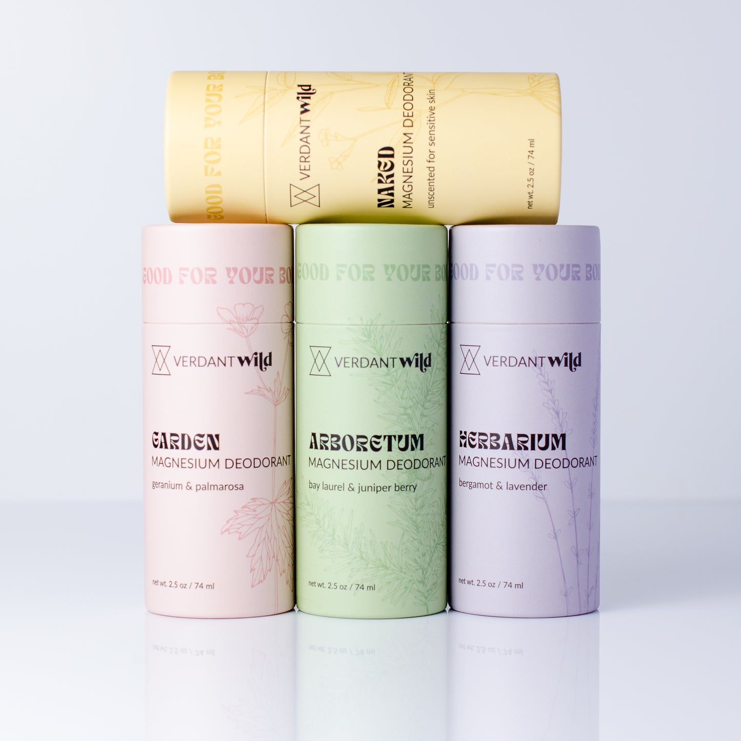 Four cylindrical Verdant Wild magnesium deodorant tubes arranged in a fan shape on a white reflective surface. The top tube is yellow, while the three tubes below are pastel pink, light green, and lavender.