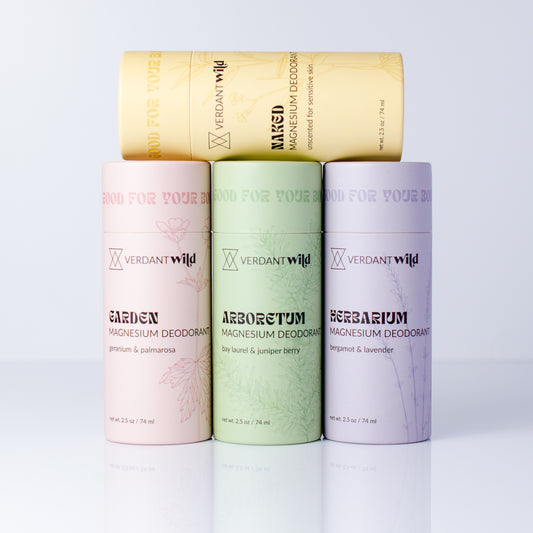 Four cylindrical Verdant Wild magnesium deodorant tubes arranged in a fan shape on a white reflective surface. The top tube is yellow, while the three tubes below are pastel pink, light green, and lavender.