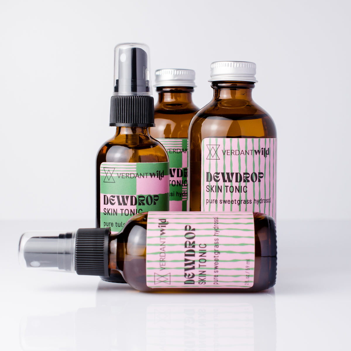 Four amber glass bottles of Verdant Wild Dewdrop Skin Tonic arranged on a white reflective surface against a light gray background.