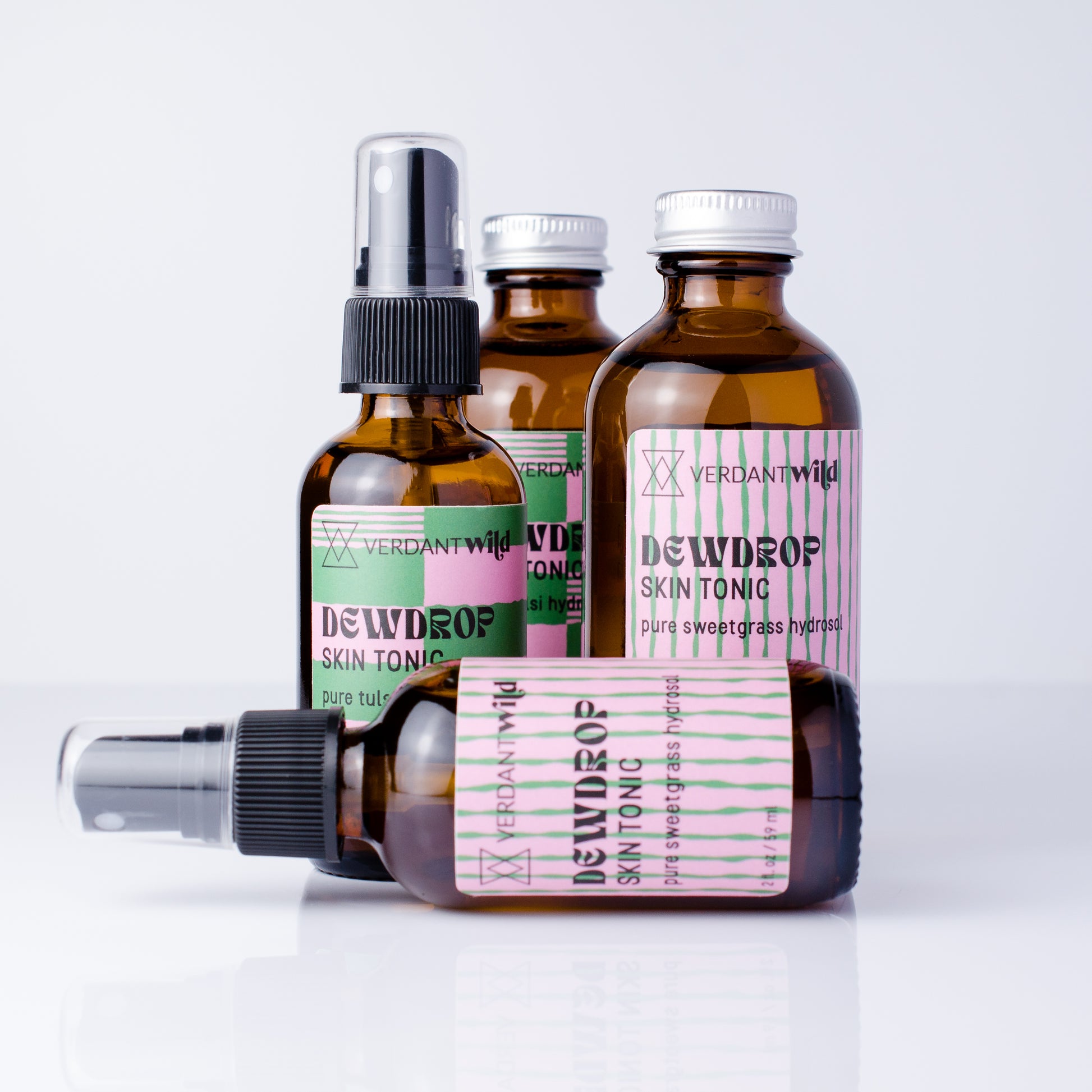 4 glass amber bottles of Verdant Wild Dewdrop Skin Tonic arranged on a white reflective surface against a light gray background, with one bottle lying down in front and 3 standing behind.