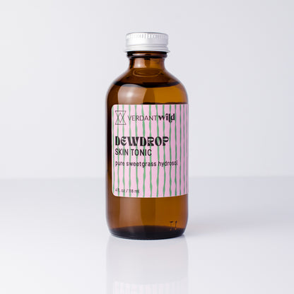 A 4 fl oz amber glass bottle of Verdant Wild Dewdrop Skin Tonic with a silver cap and a pink and green striped label, set against a clean white background.