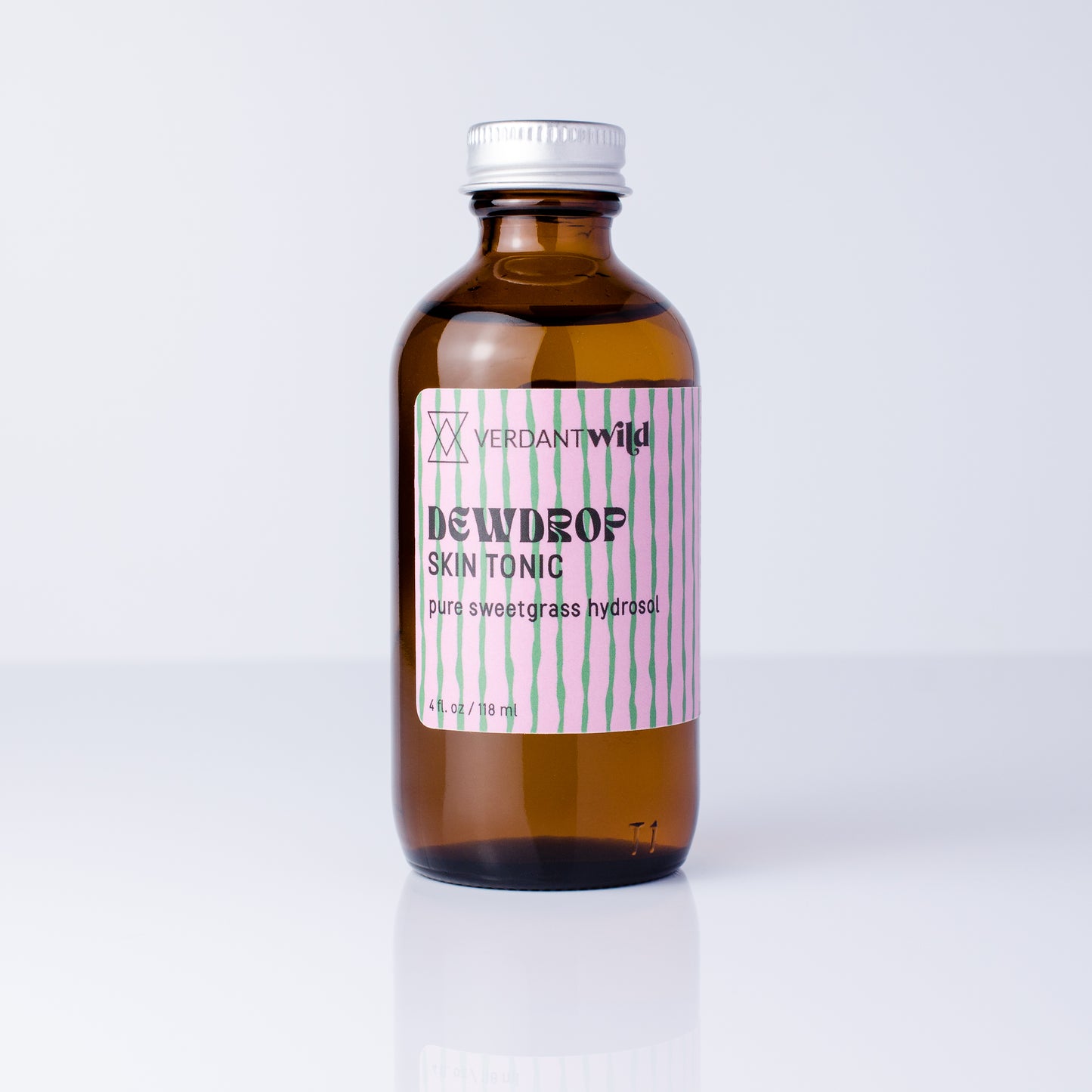 An amber glass bottle of Verdant Wild Sweetgrass Skin Tonic with a silver cap and a pink and green striped label, set against a clean white background.