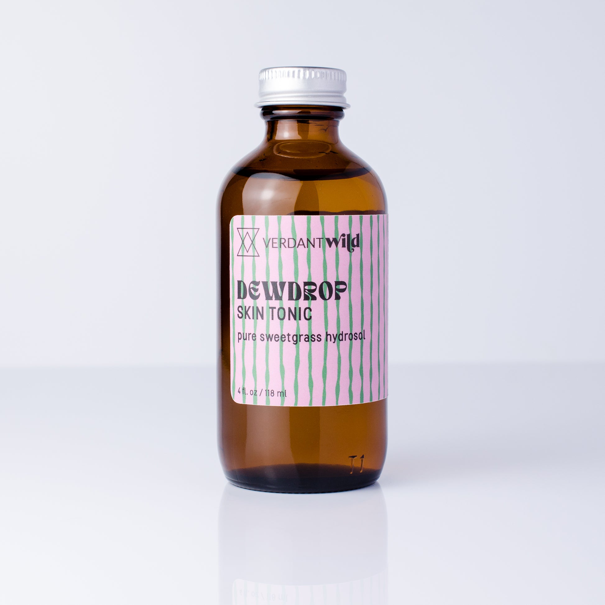 An amber glass bottle of Verdant Wild Sweetgrass Skin Tonic with a silver cap and a pink and green striped label, set against a clean white background.