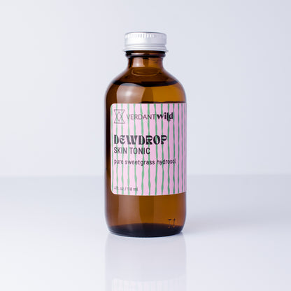 An amber glass bottle of Verdant Wild Sweetgrass Skin Tonic with a silver cap and a pink and green striped label, set against a clean white background.