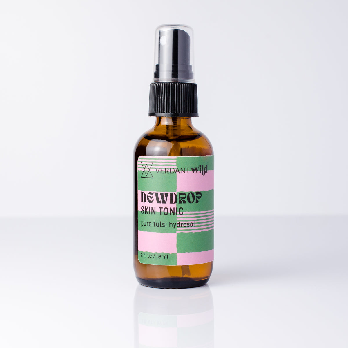 A 2 fl oz amber glass spray bottle of Verdant Wild Dewdrop Skin Tonic with a black spray cap and a colorful pink, green, and white label, set against a clean white background with a soft reflection.