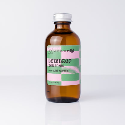 An amber glass bottle of Verdant Wild Dewdrop Skin Tonic with a silver cap and a pink, green, and white label, set against a clean white background.