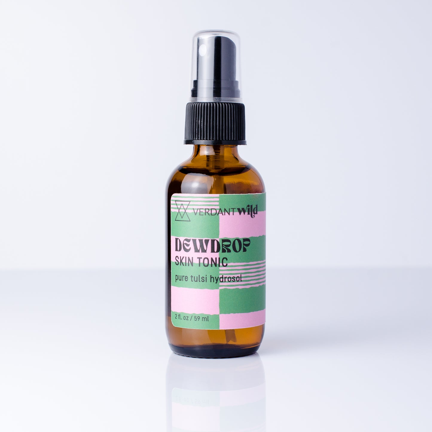 A 2 fl oz amber glass spray bottle of Verdant Wild Tulsi Skin Tonic with a black spray cap and a pastel pink, green, and white label, set against a clean white background with a soft reflection.