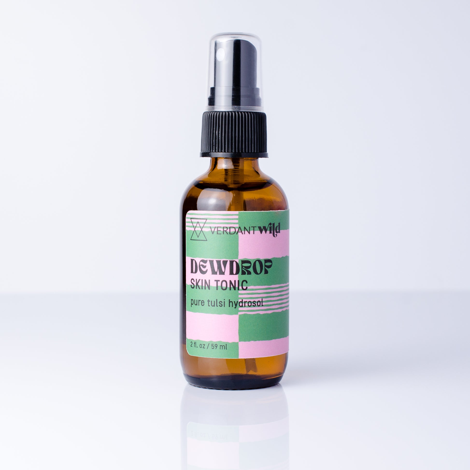 A 2 fl oz amber glass spray bottle of Verdant Wild Tulsi Skin Tonic with a black spray cap and a pastel pink, green, and white label, set against a clean white background with a soft reflection.